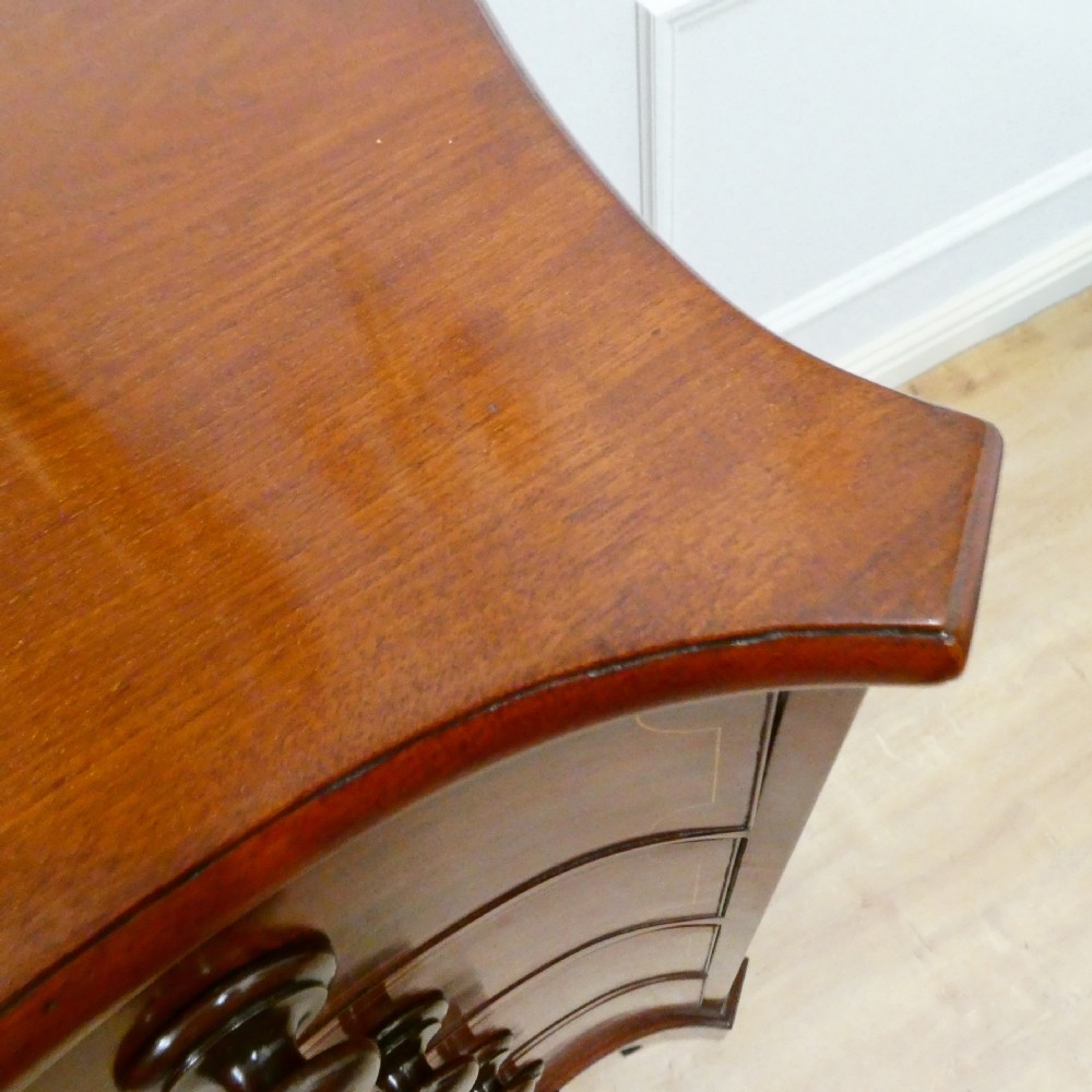 A Georgian mahogany chest of drawers featuring a serpentine front, four graduated drawers with turned wooden knobs, fine line inlay, and bracket feet. View VI