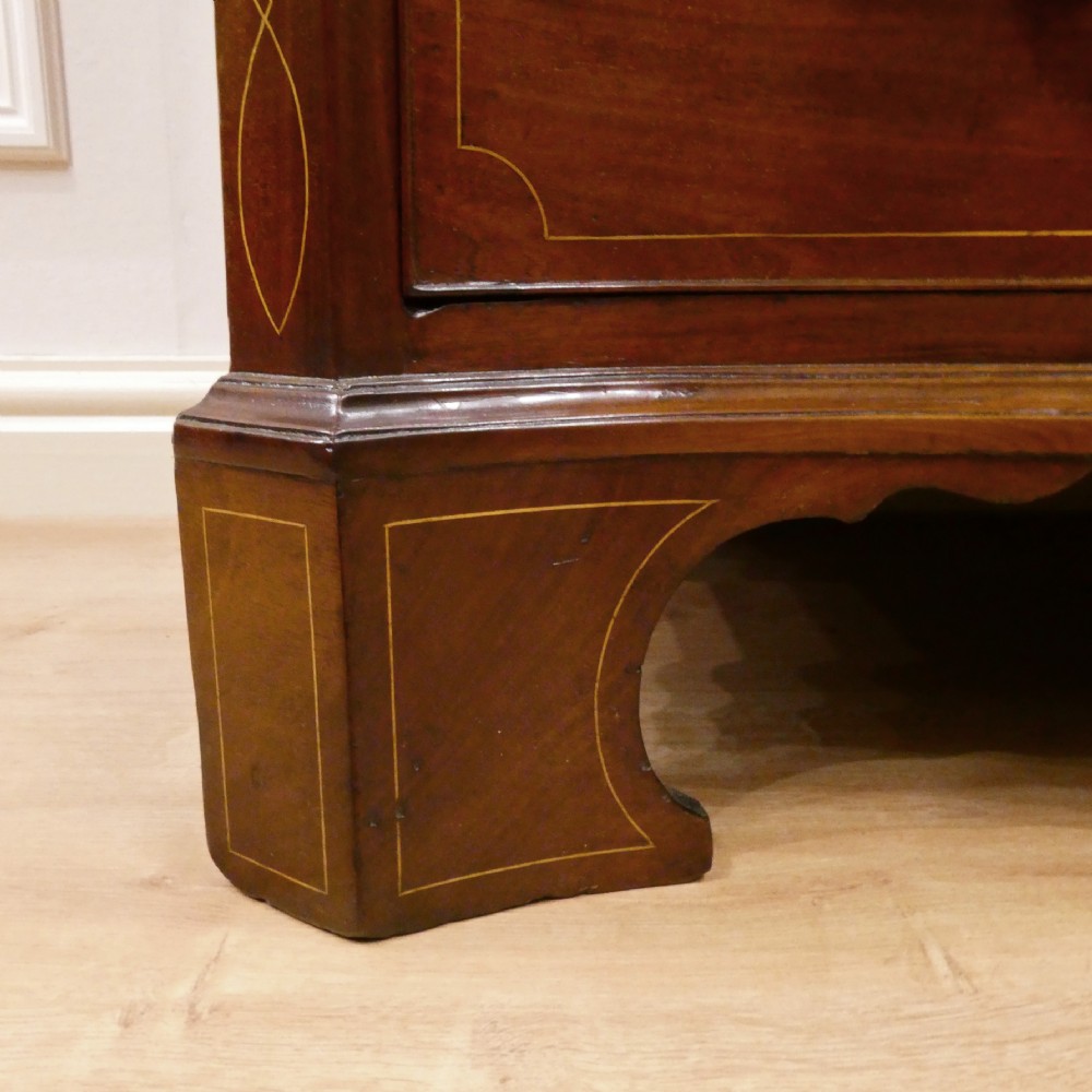 A Georgian mahogany chest of drawers featuring a serpentine front, four graduated drawers with turned wooden knobs, fine line inlay, and bracket feet. View VII