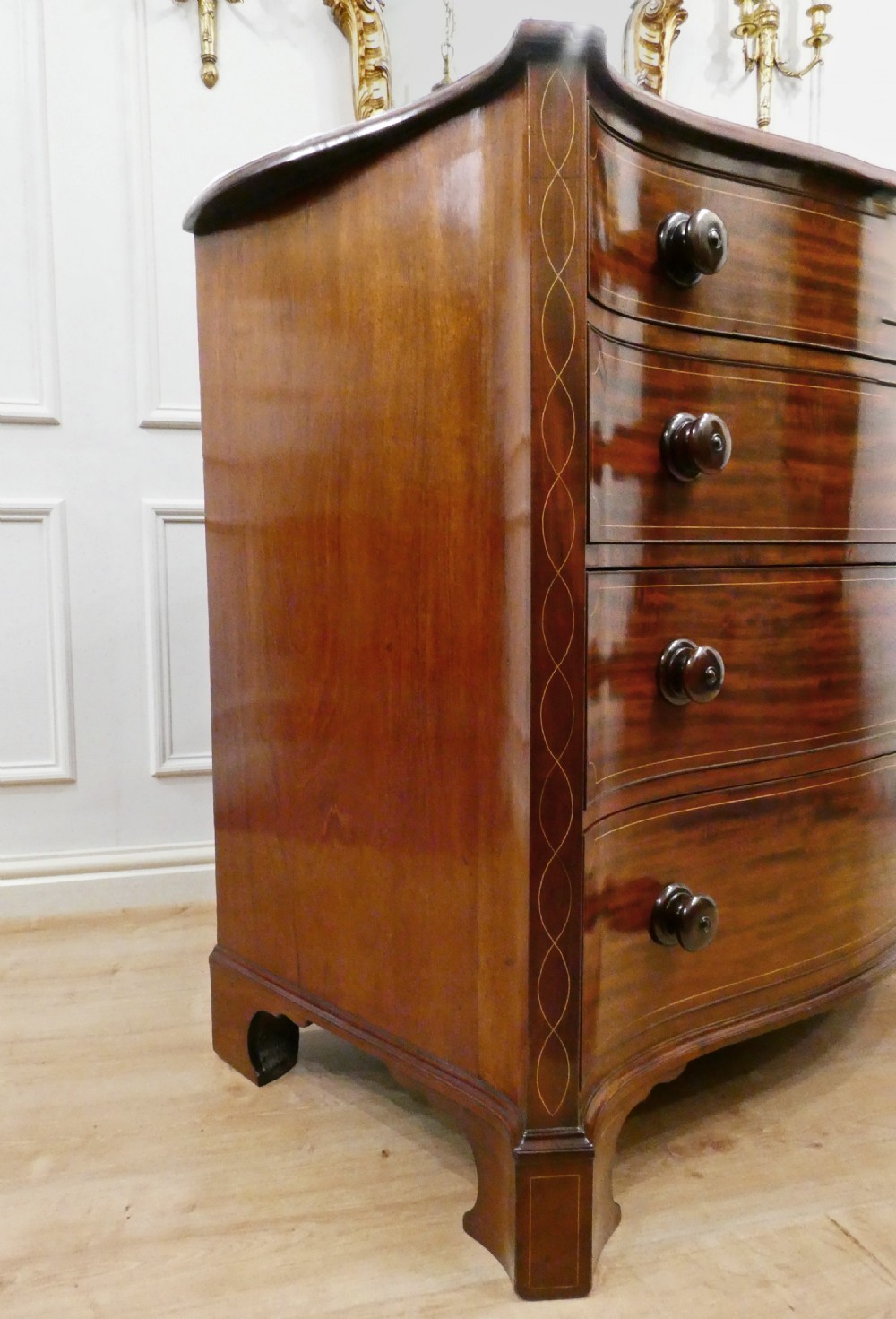 A Georgian mahogany chest of drawers featuring a serpentine front, four graduated drawers with turned wooden knobs, fine line inlay, and bracket feet. View IX