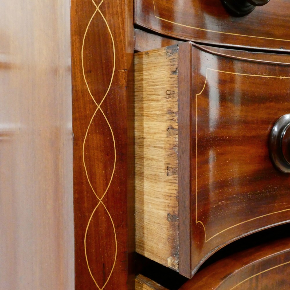 A Georgian mahogany chest of drawers featuring a serpentine front, four graduated drawers with turned wooden knobs, fine line inlay, and bracket feet. View X