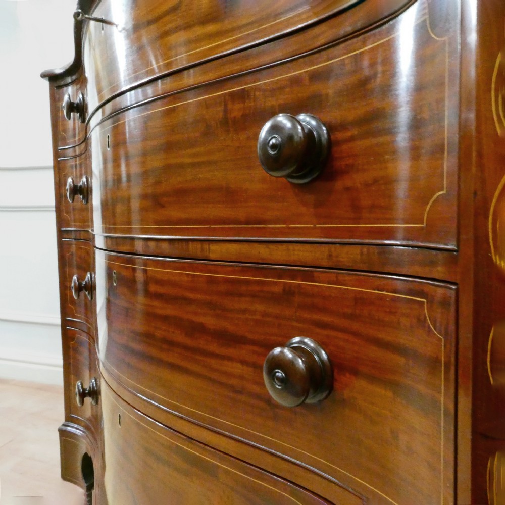 A Georgian mahogany chest of drawers featuring a serpentine front, four graduated drawers with turned wooden knobs, fine line inlay, and bracket feet. View XII