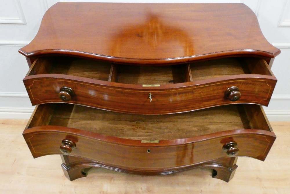 A Georgian mahogany chest of drawers featuring a serpentine front, four graduated drawers with turned wooden knobs, fine line inlay, and bracket feet. View XIII