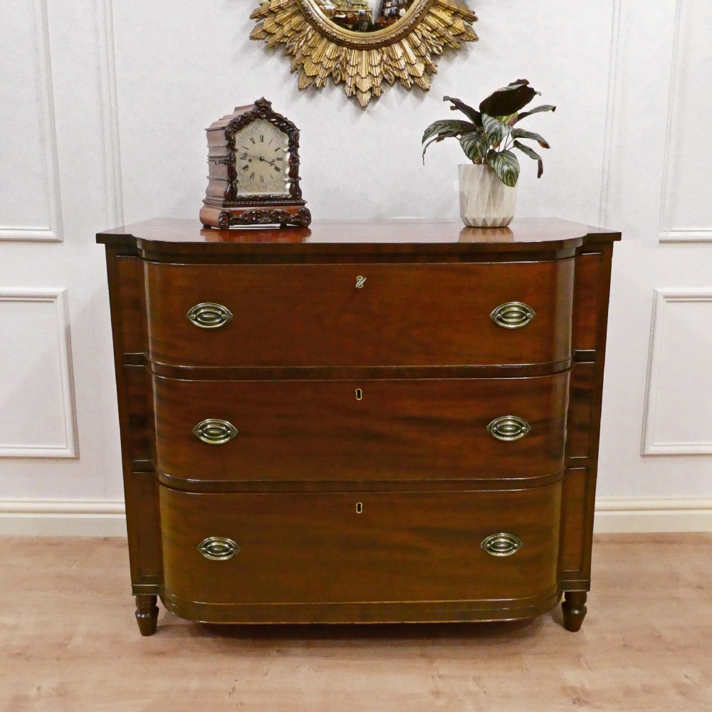 A Regency period mahogany bow-fronted chest of drawers featuring three graduated drawers with brass oval handles and short turned feet.