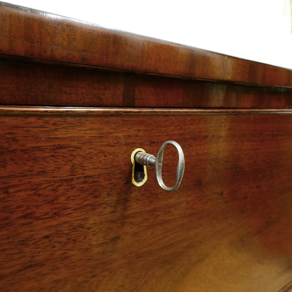 A Regency period mahogany bow-fronted chest of drawers featuring three graduated drawers with brass oval handles and short turned feet. View IV