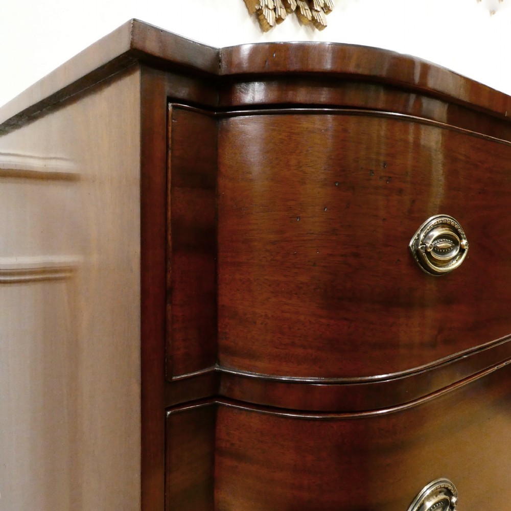 A Regency period mahogany bow-fronted chest of drawers featuring three graduated drawers with brass oval handles and short turned feet. View V