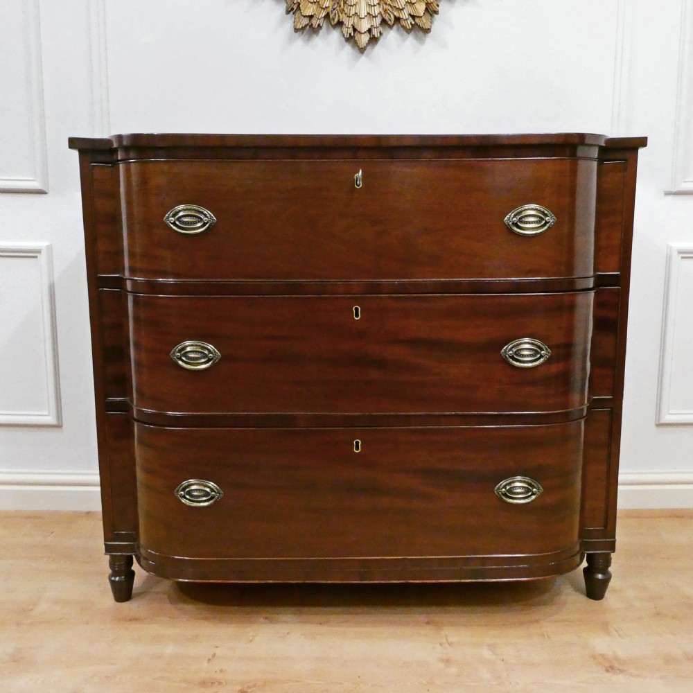 A Regency period mahogany bow-fronted chest of drawers featuring three graduated drawers with brass oval handles and short turned feet. View XI
