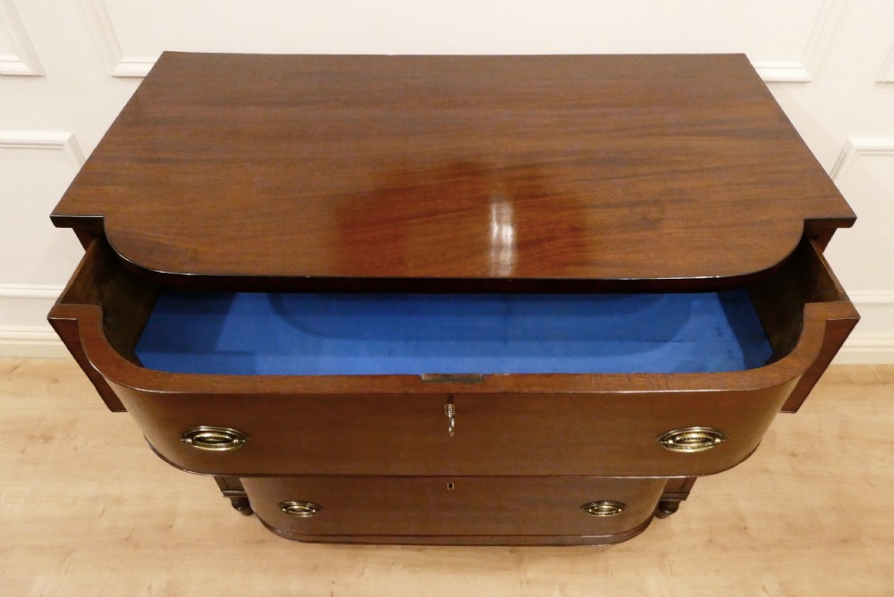 A Regency period mahogany bow-fronted chest of drawers featuring three graduated drawers with brass oval handles and short turned feet. View XII
