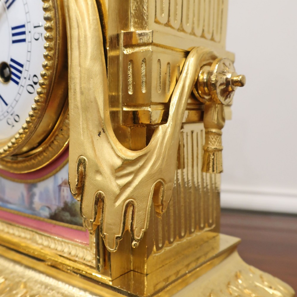 A French gilt bronze mantel clock featuring an urn top finial, pink hand-painted porcelain panels, and a white enamel dial with Roman numerals. View VIII