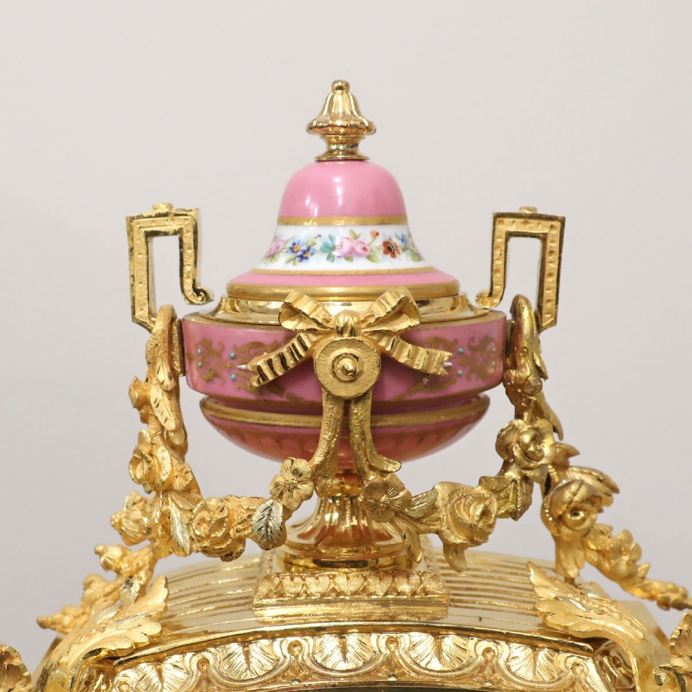 A French gilt bronze mantel clock featuring an urn top finial, pink hand-painted porcelain panels, and a white enamel dial with Roman numerals. View IX