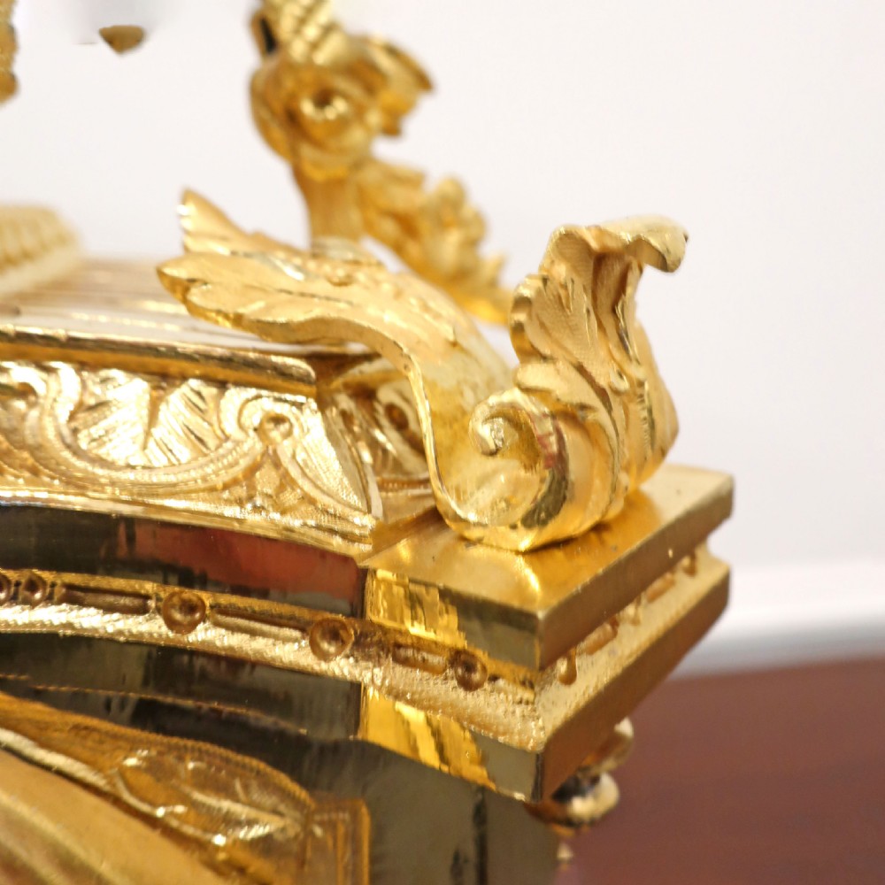 A French gilt bronze mantel clock featuring an urn top finial, pink hand-painted porcelain panels, and a white enamel dial with Roman numerals. View XII
