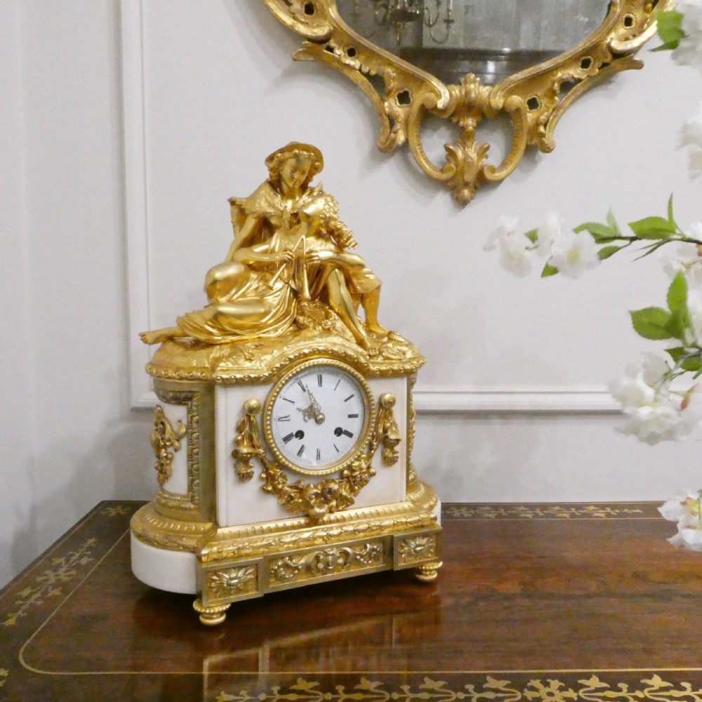 A French gilt bronze and white marble mantel clock featuring a classical figural sculpture on top and decorative floral mounts around the dial.