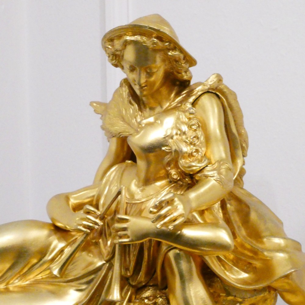A French gilt bronze and white marble mantel clock featuring a classical figural sculpture on top and decorative floral mounts around the dial. View V