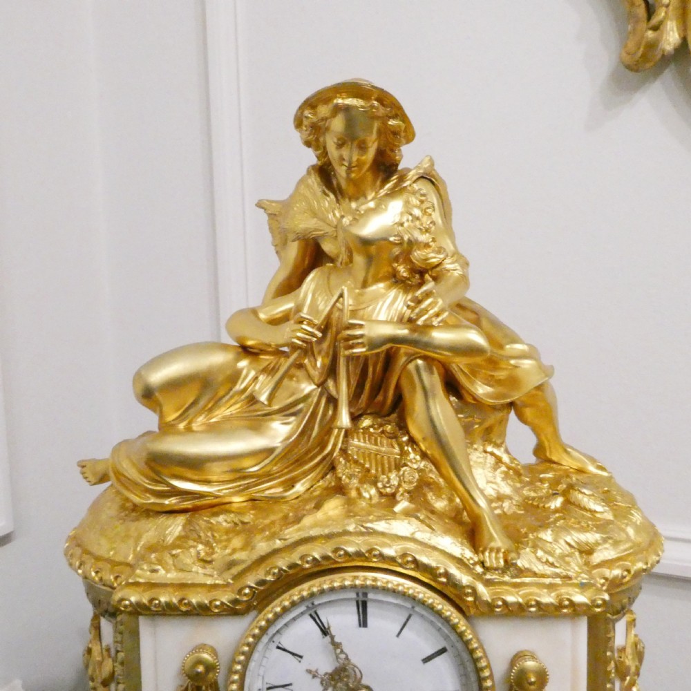 A French gilt bronze and white marble mantel clock featuring a classical figural sculpture on top and decorative floral mounts around the dial. View VI