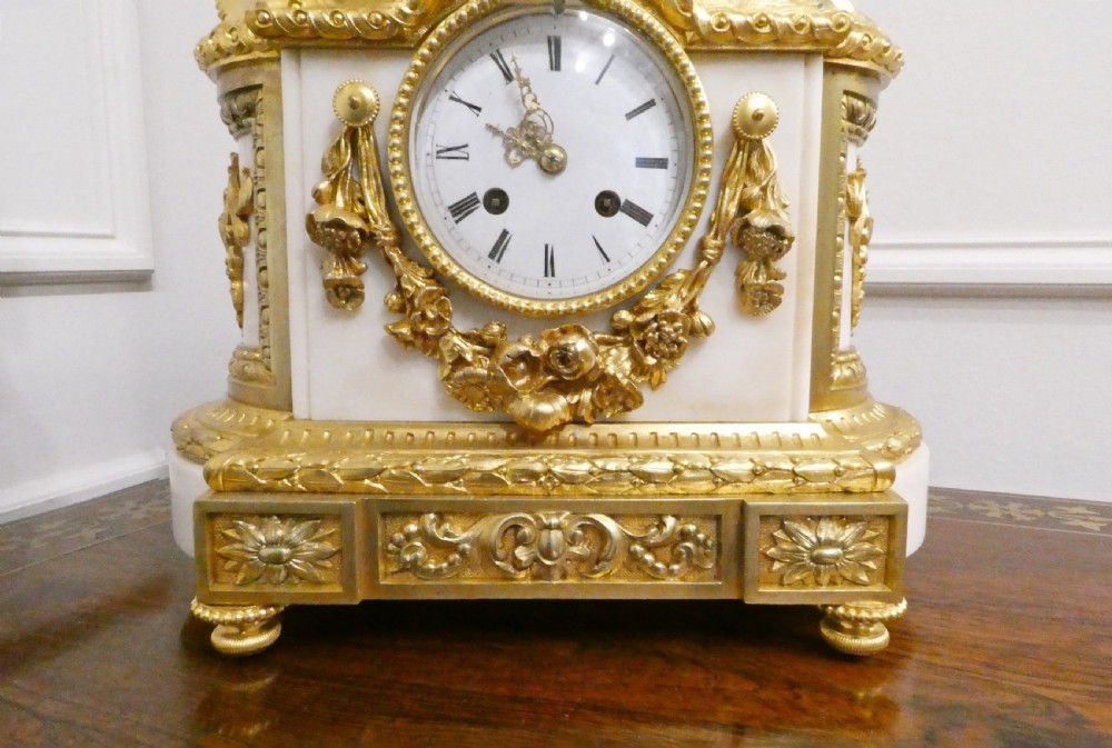 A French gilt bronze and white marble mantel clock featuring a classical figural sculpture on top and decorative floral mounts around the dial. View IX