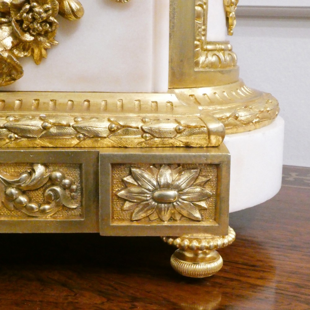 A French gilt bronze and white marble mantel clock featuring a classical figural sculpture on top and decorative floral mounts around the dial. View X
