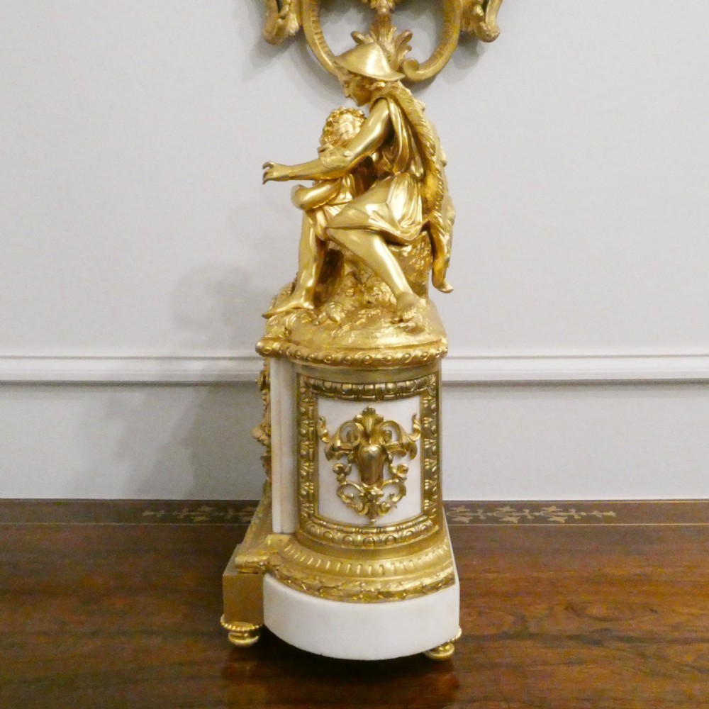 A French gilt bronze and white marble mantel clock featuring a classical figural sculpture on top and decorative floral mounts around the dial. View XI