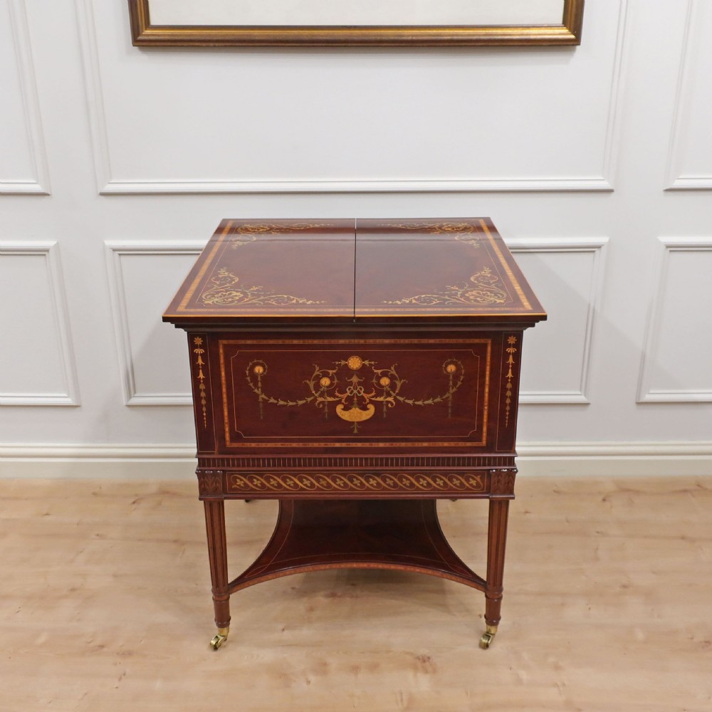 An Edwardian mahogany drinks table featuring intricate satinwood marquetry inlays, a split-top opening lid, tapered legs, and brass castors.