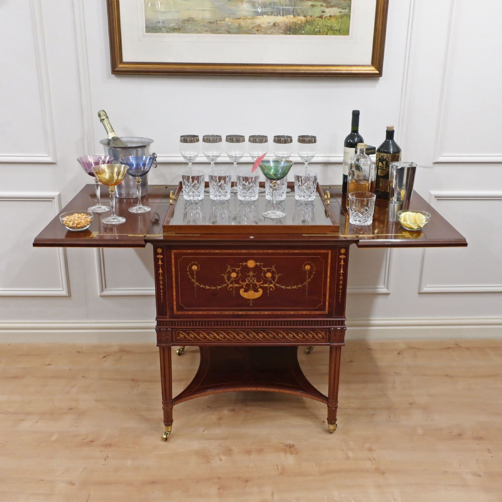 An Edwardian mahogany drinks table featuring intricate satinwood marquetry inlays, a split-top opening lid, tapered legs, and brass castors. View II