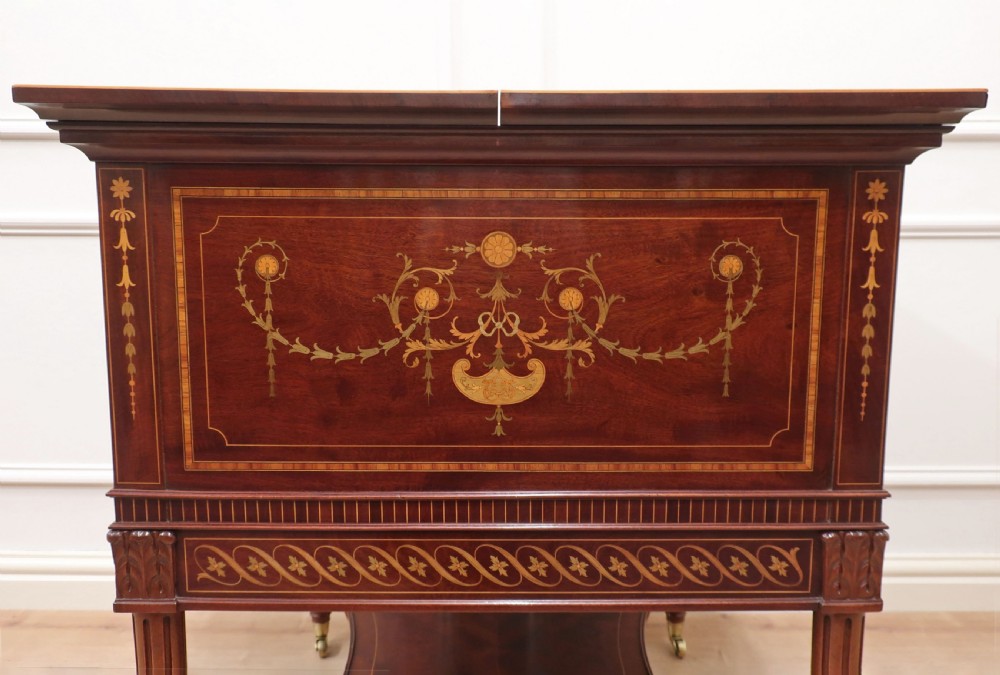 An Edwardian mahogany drinks table featuring intricate satinwood marquetry inlays, a split-top opening lid, tapered legs, and brass castors. View VI