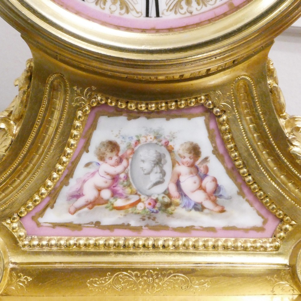 A French Louis XV style gilt bronze mantel clock featuring a hand-painted porcelain dial, lower cherub panel, scroll feet, and an ornamental urn finial. View V