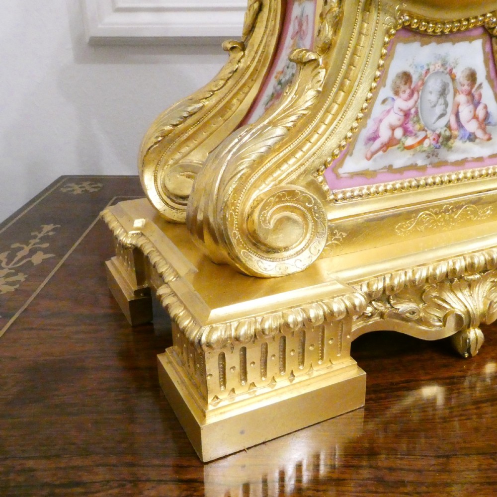 A French Louis XV style gilt bronze mantel clock featuring a hand-painted porcelain dial, lower cherub panel, scroll feet, and an ornamental urn finial. View VII