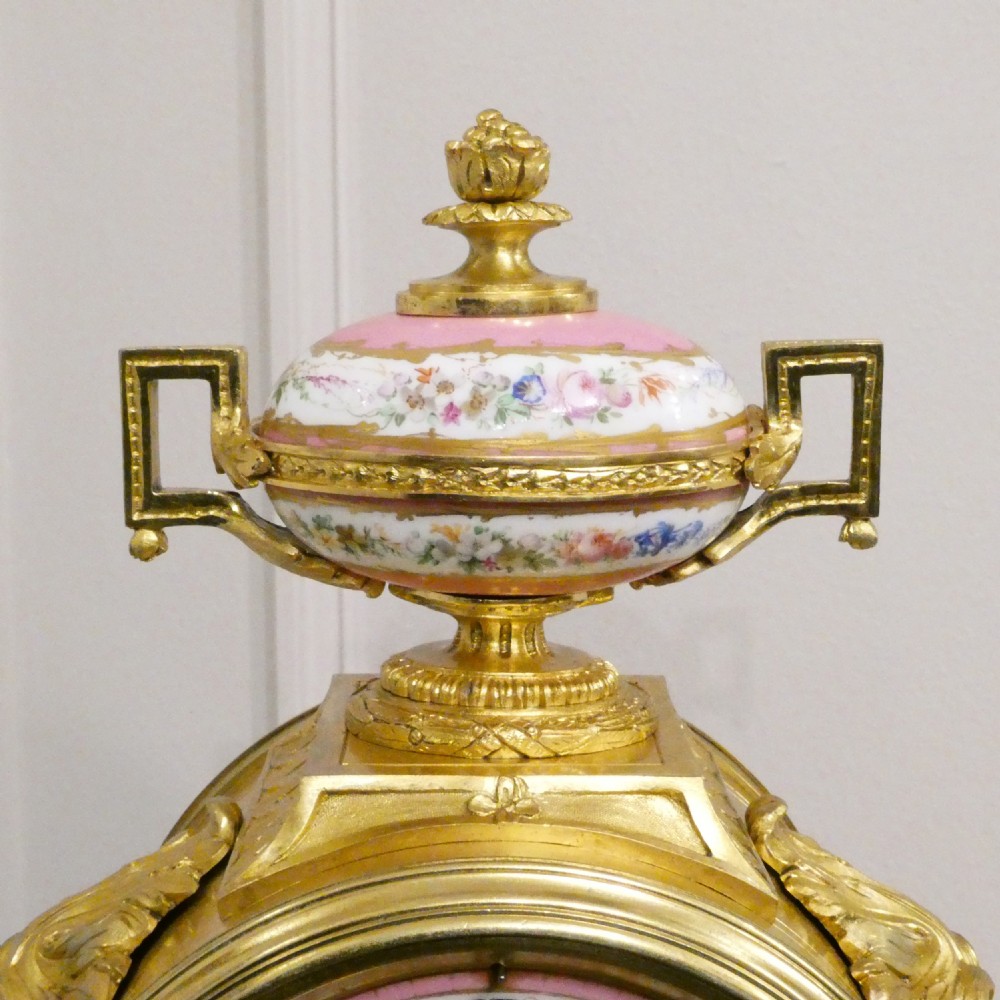 A French Louis XV style gilt bronze mantel clock featuring a hand-painted porcelain dial, lower cherub panel, scroll feet, and an ornamental urn finial. View VIII
