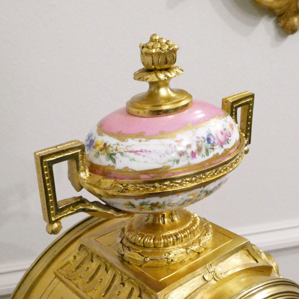 A French Louis XV style gilt bronze mantel clock featuring a hand-painted porcelain dial, lower cherub panel, scroll feet, and an ornamental urn finial. View X