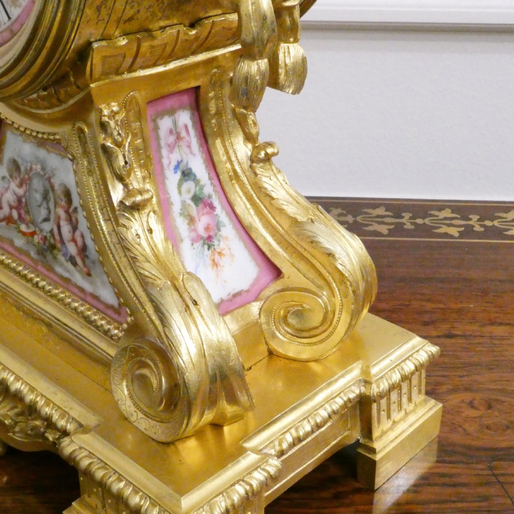 A French Louis XV style gilt bronze mantel clock featuring a hand-painted porcelain dial, lower cherub panel, scroll feet, and an ornamental urn finial. View XII