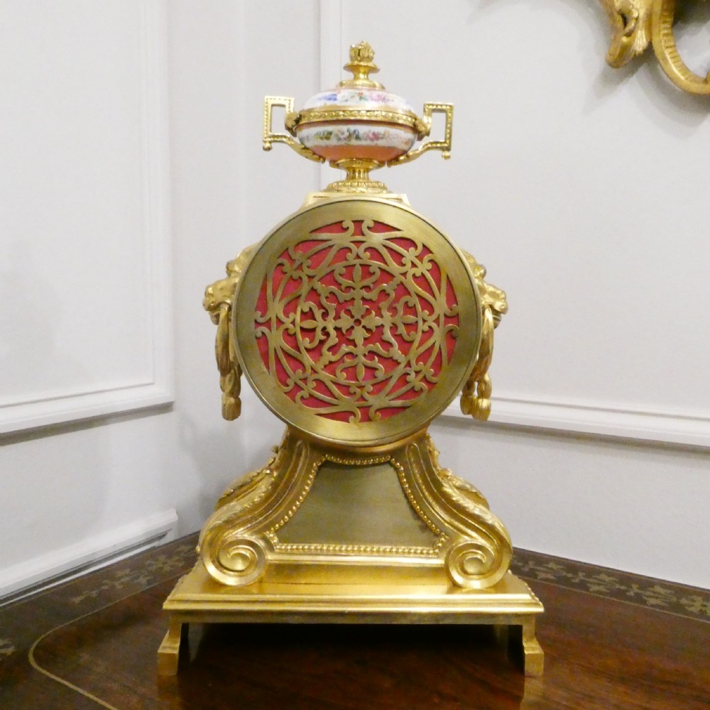 A French Louis XV style gilt bronze mantel clock featuring a hand-painted porcelain dial, lower cherub panel, scroll feet, and an ornamental urn finial. View XIV