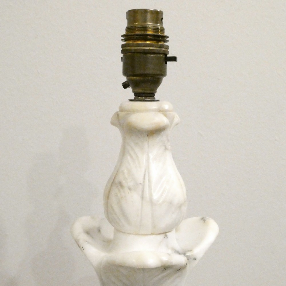 An early 20th-century carved white alabaster table lamp featuring an urn-shaped stem, square plinth base, and a pleated white fabric lampshade. View VI