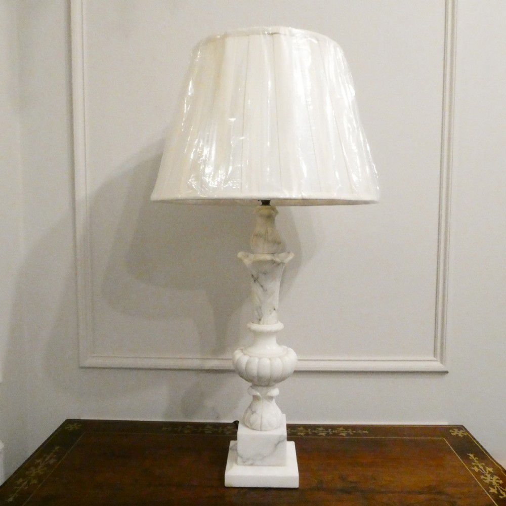 An early 20th-century carved white alabaster table lamp featuring an urn-shaped stem, square plinth base, and a pleated white fabric lampshade. View VIII