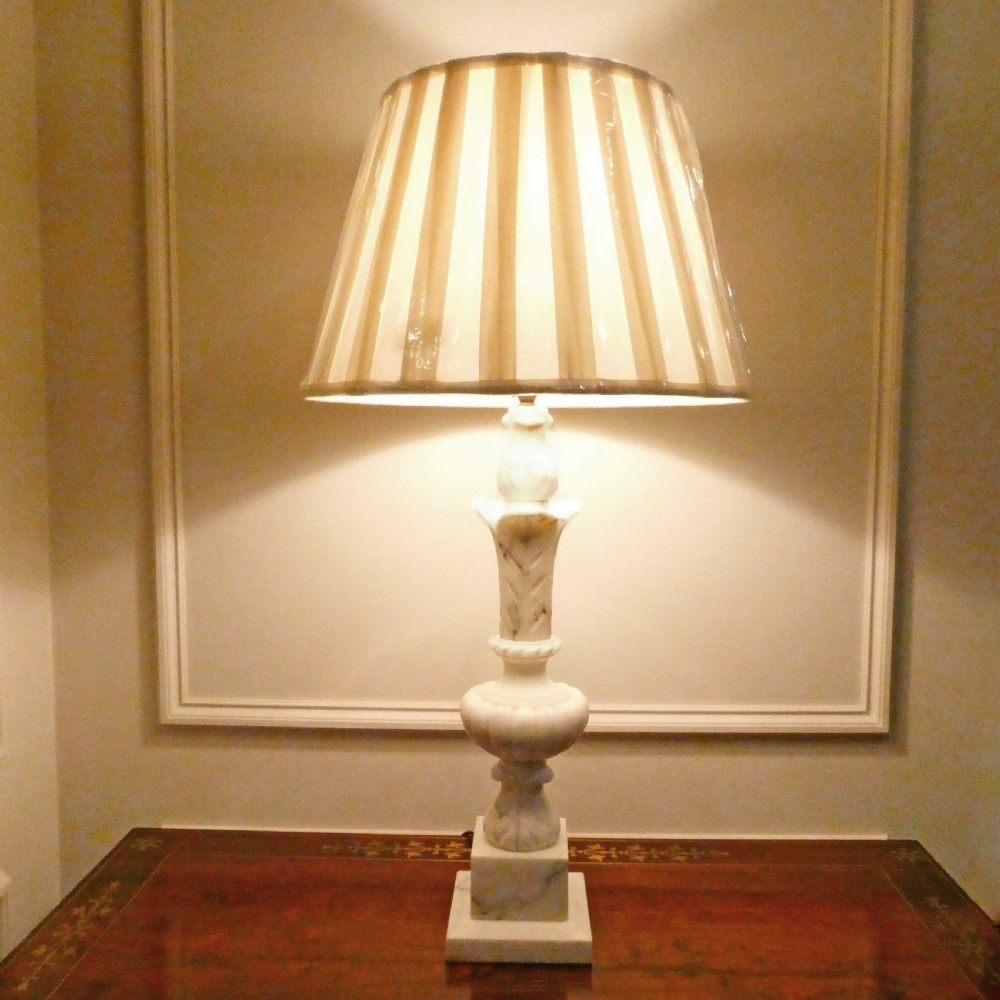 An early 20th-century carved white alabaster table lamp featuring an urn-shaped stem, square plinth base, and a pleated white fabric lampshade. View IX