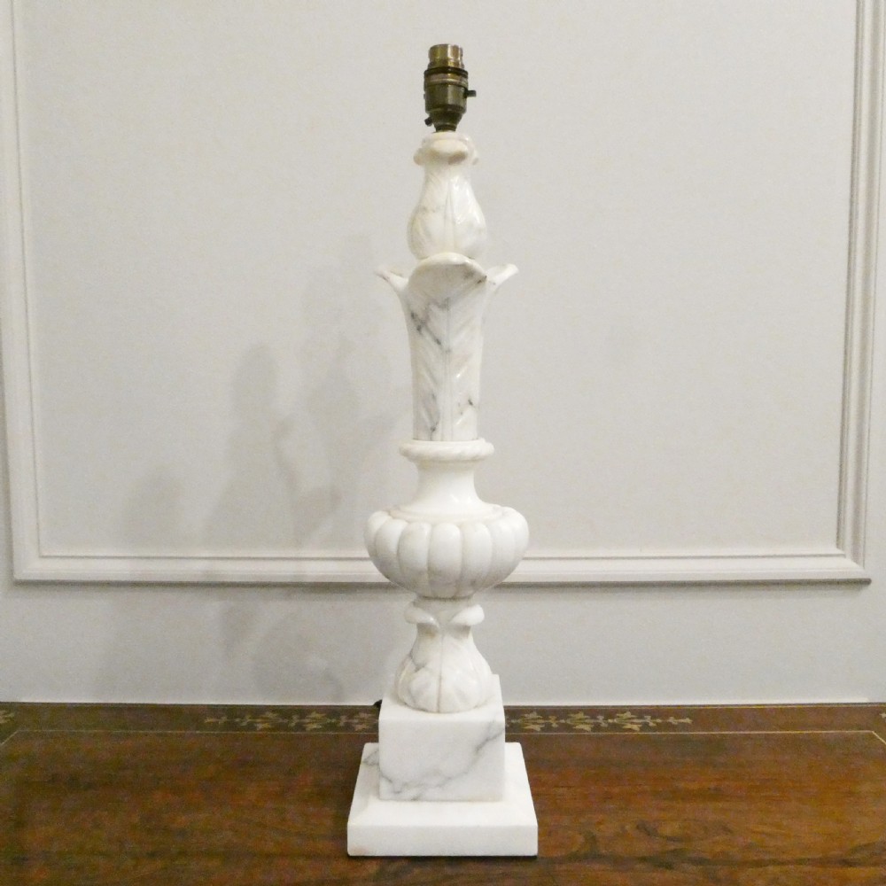 An early 20th-century carved white alabaster table lamp featuring an urn-shaped stem, square plinth base, and a pleated white fabric lampshade. View X