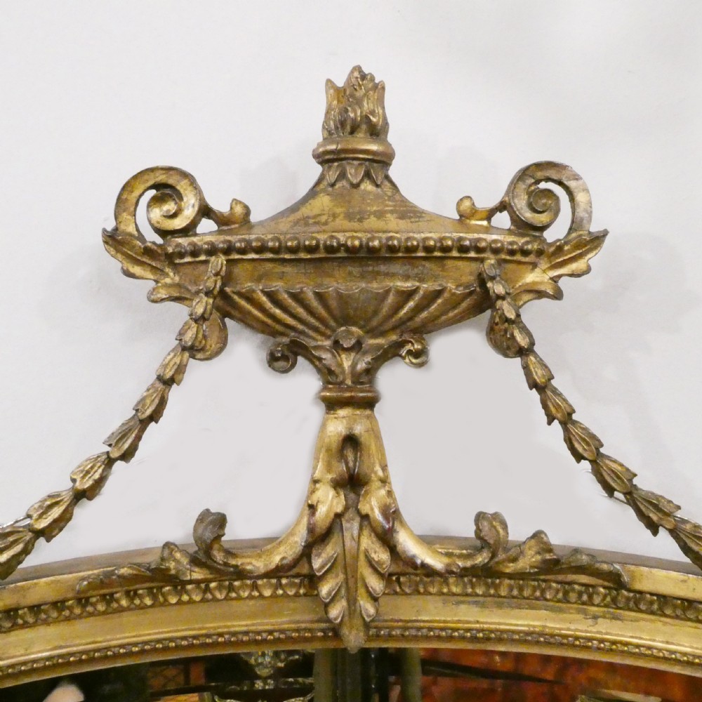 An oval giltwood wall mirror featuring Neoclassical urn cresting, suspended husk festoons with bow ribbons, and lower decorative scrollwork. View II