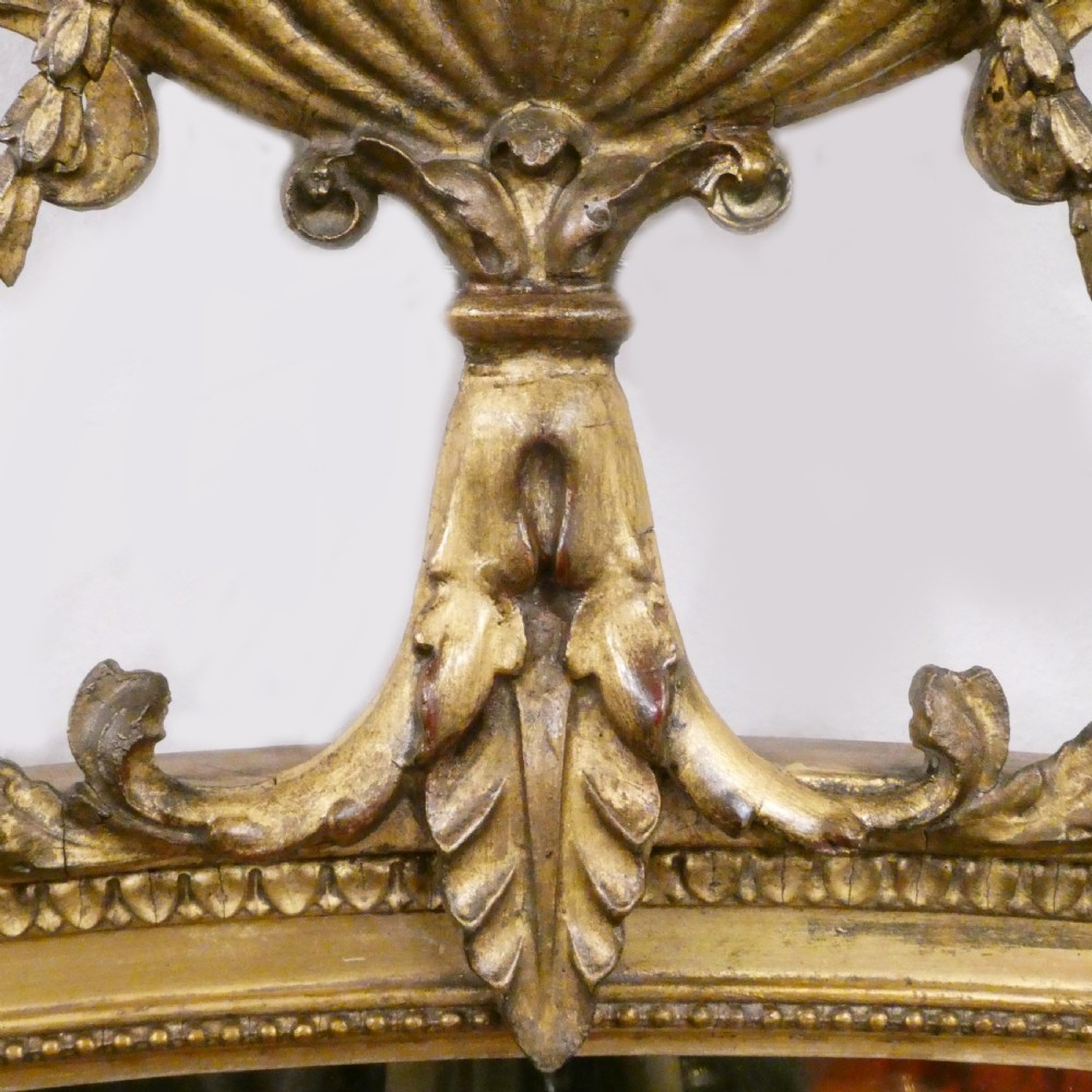 An oval giltwood wall mirror featuring Neoclassical urn cresting, suspended husk festoons with bow ribbons, and lower decorative scrollwork. View III