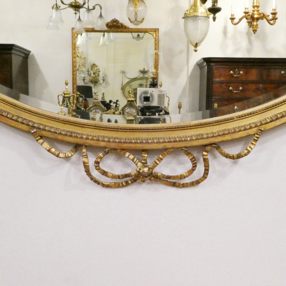 An oval giltwood wall mirror featuring Neoclassical urn cresting, suspended husk festoons with bow ribbons, and lower decorative scrollwork. View IX