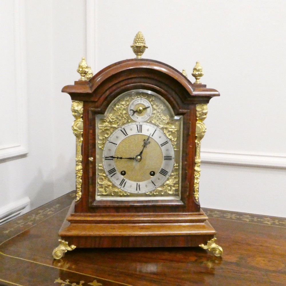 A dark mahogany arched bracket clock featuring gilt brass corner mounts, finials, and a silvered chapter ring dial with brass spandrels. View II