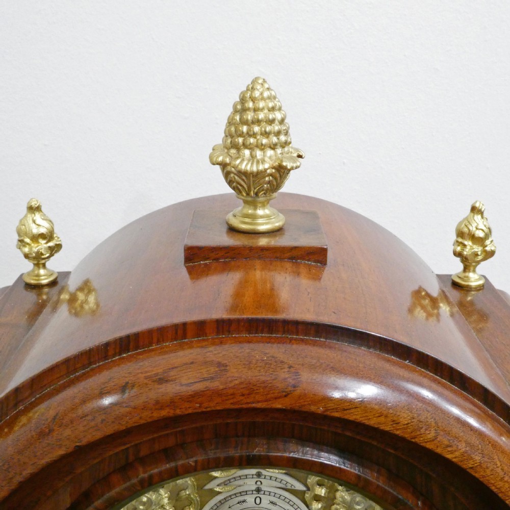 A dark mahogany arched bracket clock featuring gilt brass corner mounts, finials, and a silvered chapter ring dial with brass spandrels. View VII