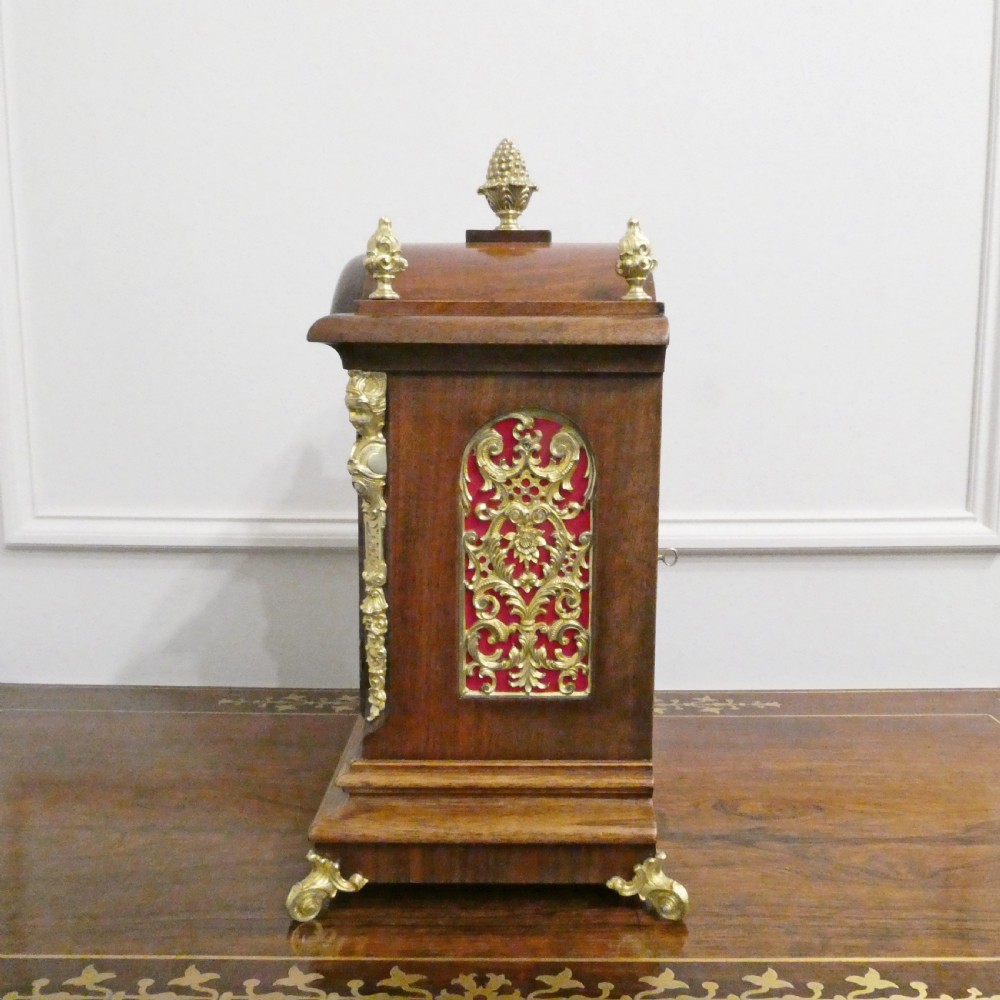 A dark mahogany arched bracket clock featuring gilt brass corner mounts, finials, and a silvered chapter ring dial with brass spandrels. View VIII