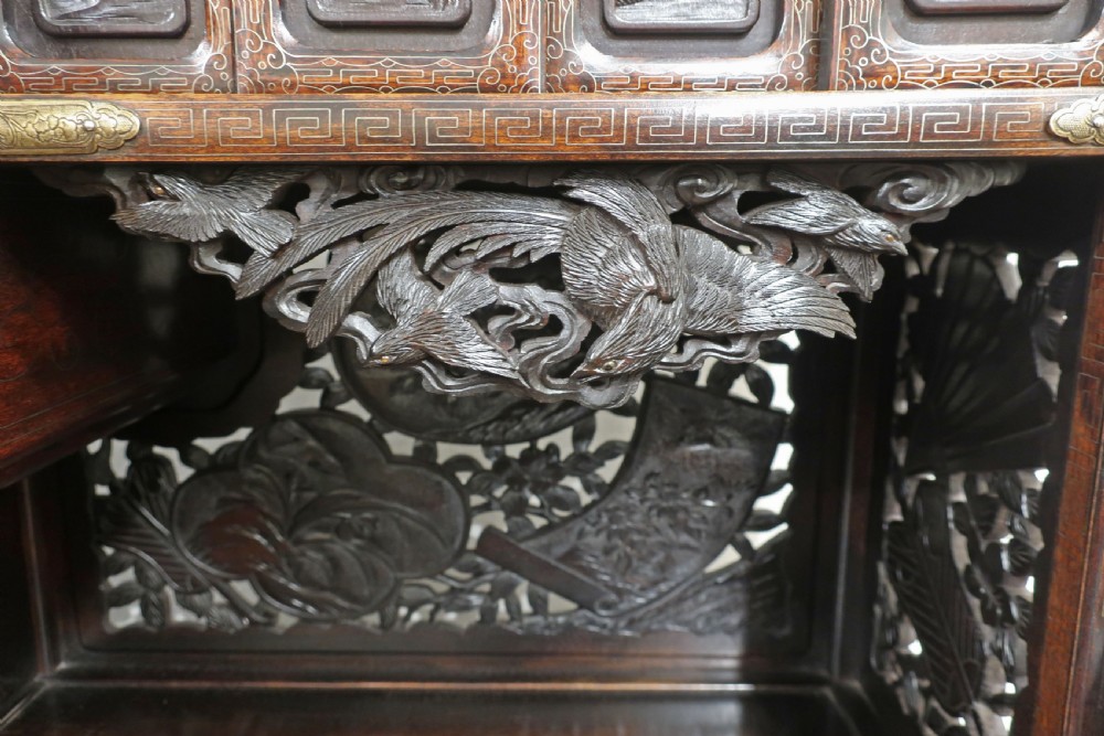 A dark carved hardwood Japanese Meiji period shodana cabinet featuring asymmetrical shelves, relief-carved panel doors, metal mounts, and a carved lower base. View VI