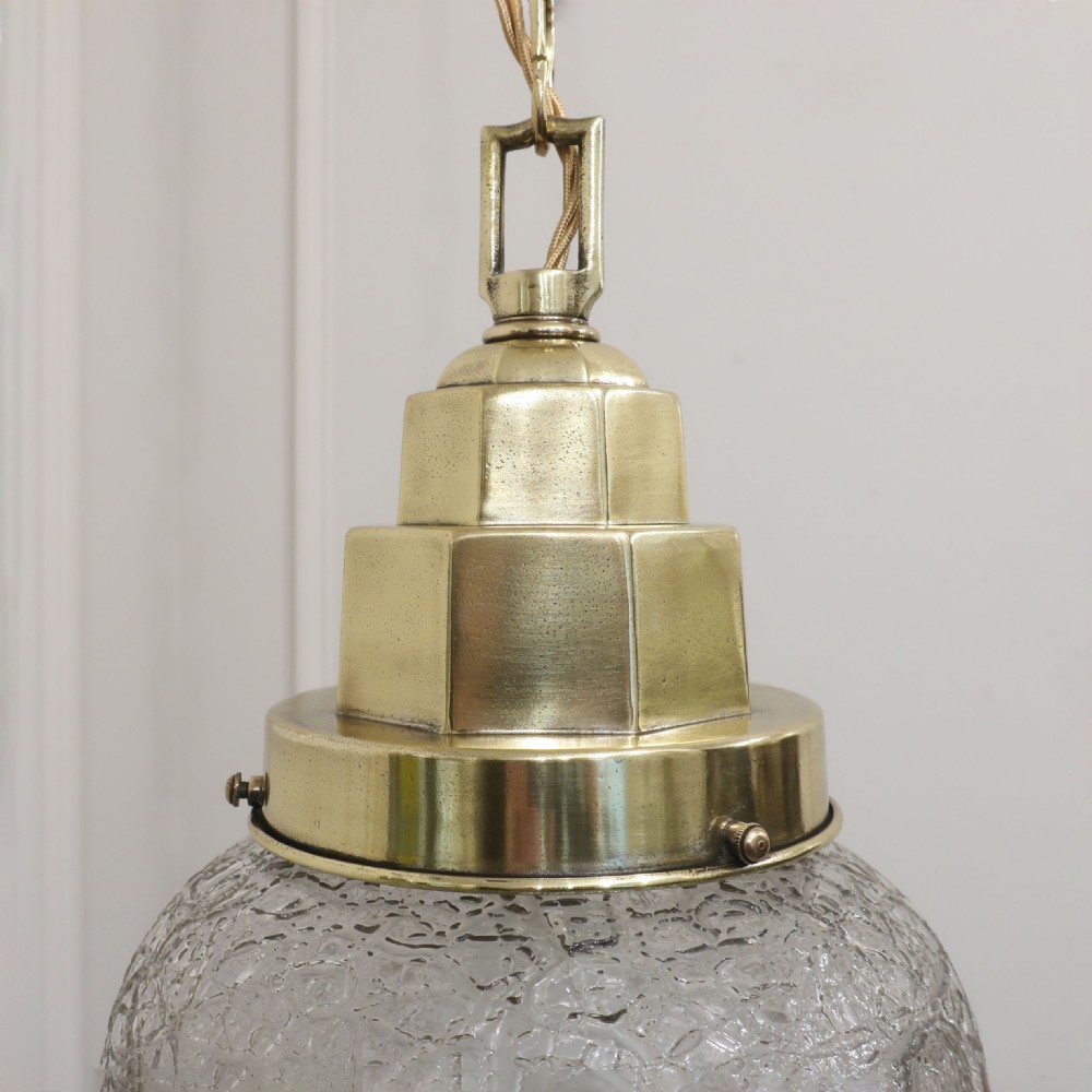 An Art Deco pendant light featuring a stepped brass gallery cap attached to a teardrop-shaped crackle glass shade hanging from a brass chain. View V
