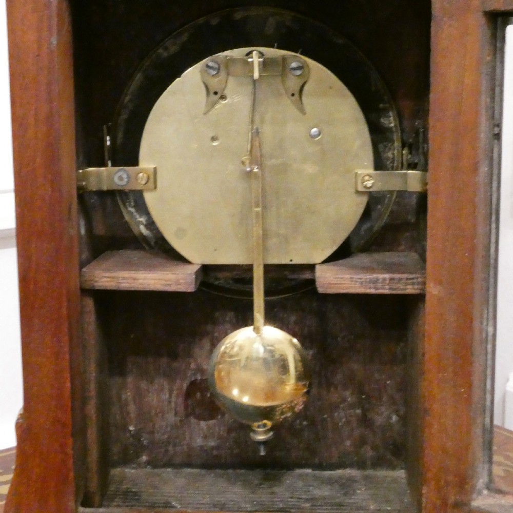 A Georgian mahogany library clock with a carved top crest, brass inlay, white dial with Roman numerals, and brass ball feet. View X