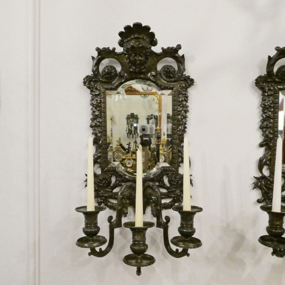 A pair of dark patinated bronze wall girandoles with ornate foliate frames surrounding central mirrored plates and three candle branches each. View II
