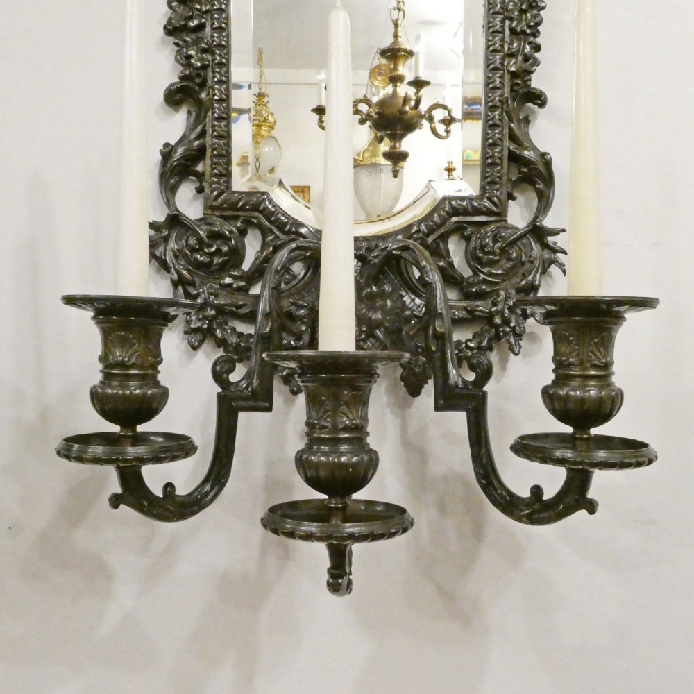 A pair of dark patinated bronze wall girandoles with ornate foliate frames surrounding central mirrored plates and three candle branches each. View IV