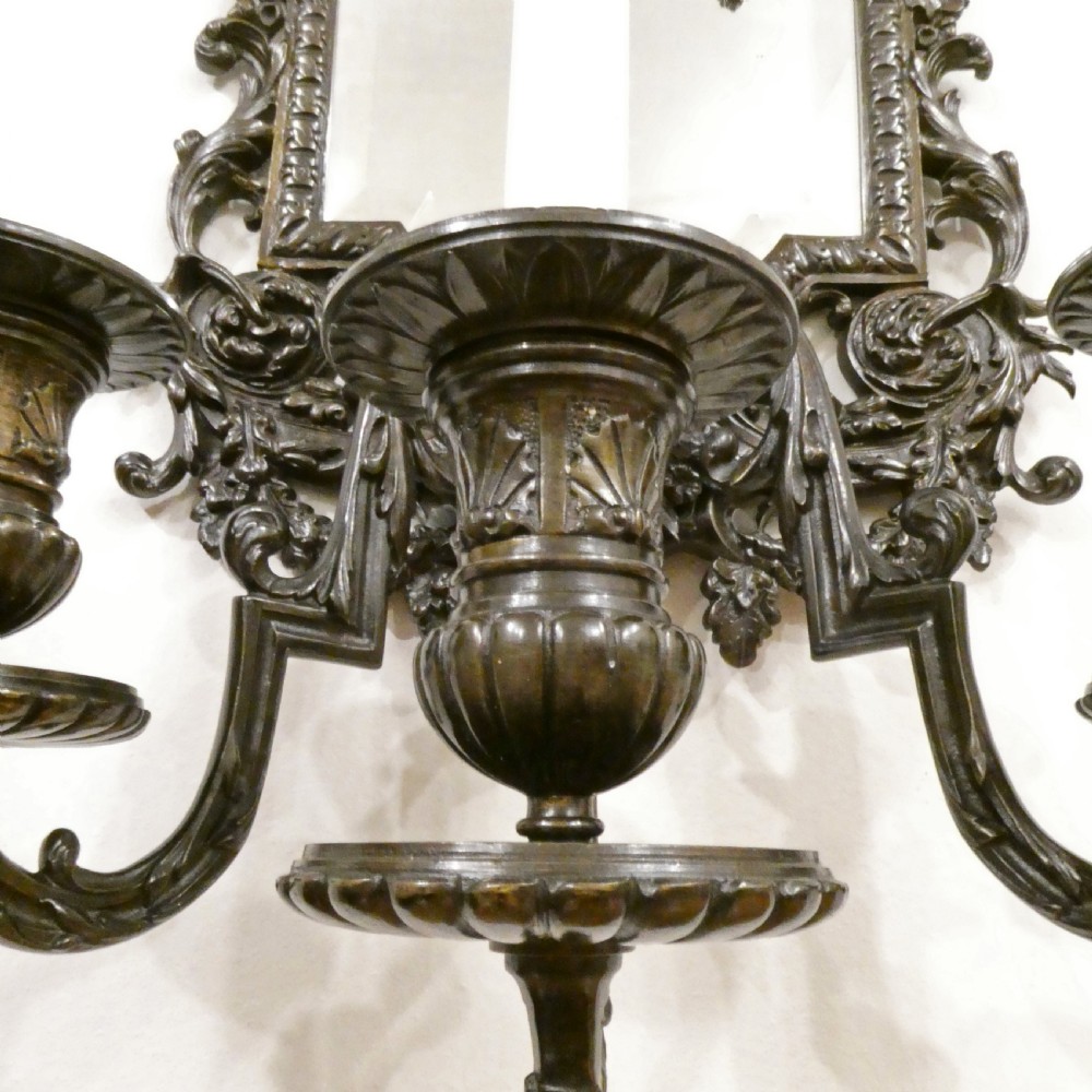 A pair of dark patinated bronze wall girandoles with ornate foliate frames surrounding central mirrored plates and three candle branches each. View V