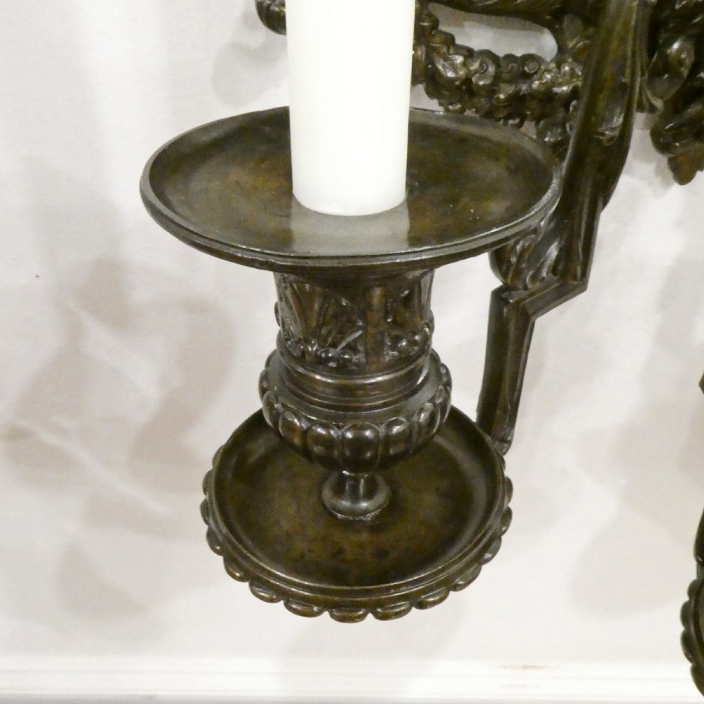 A pair of dark patinated bronze wall girandoles with ornate foliate frames surrounding central mirrored plates and three candle branches each. View VI