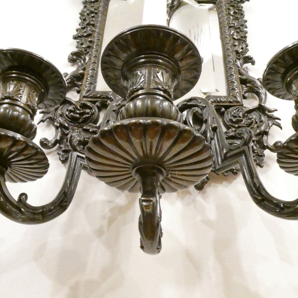 A pair of dark patinated bronze wall girandoles with ornate foliate frames surrounding central mirrored plates and three candle branches each. View VII