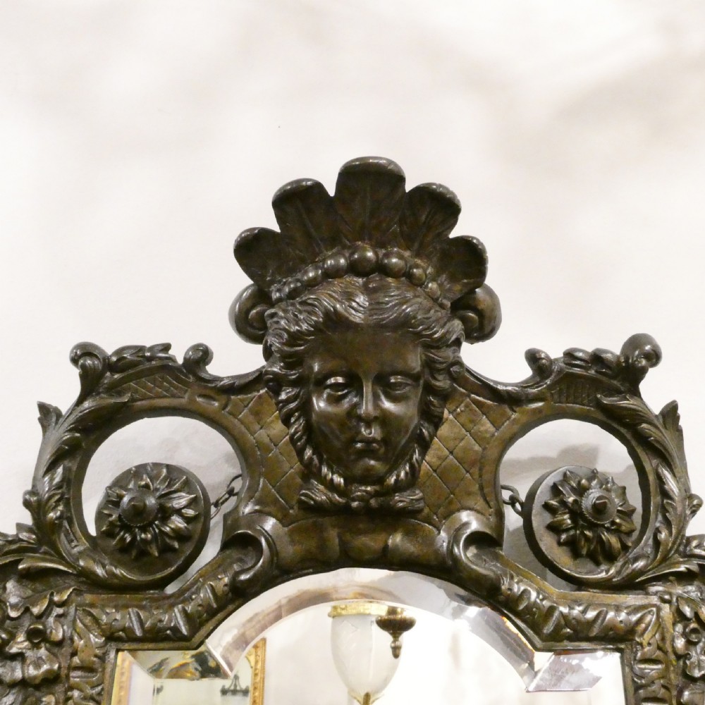 A pair of dark patinated bronze wall girandoles with ornate foliate frames surrounding central mirrored plates and three candle branches each. View X