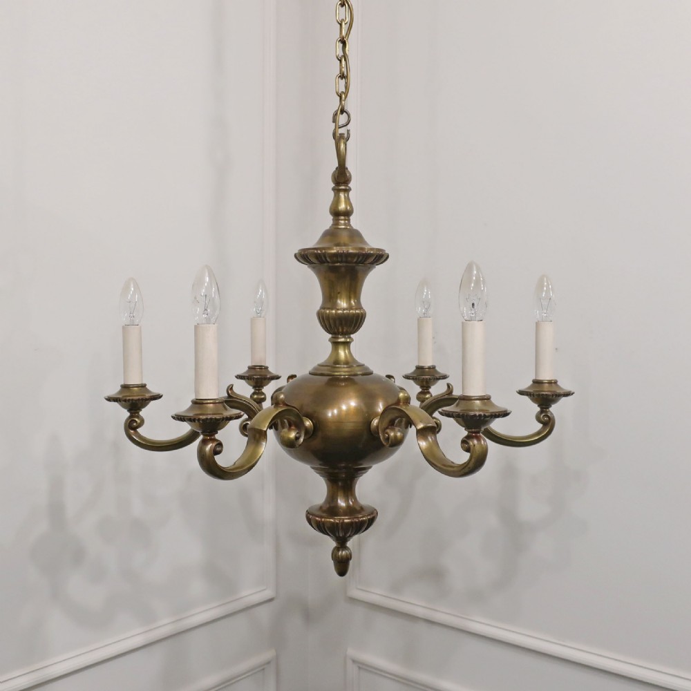 An Edwardian brass six-arm chandelier hanging from a link chain, featuring curved S-scroll branches and candle-style bulb holders.