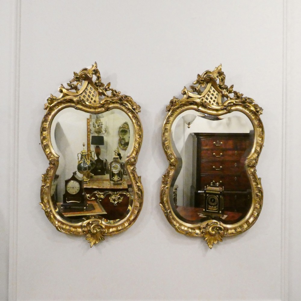 A pair of ornate French Rococo style wall mirrors featuring carved giltwood frames with scrollwork crests and lattice detailing.